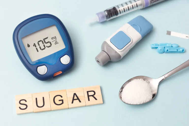A blue glucose meter showing a reading of 105 mg/dL, surrounded by diabetic monitoring tools, a spoonful of sugar, and Scrabble tiles spelling “SUGAR,” representing blood sugar monitoring and insulin resistance awareness.